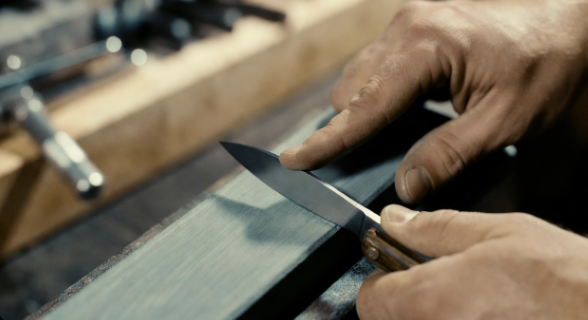 Hands sharpening a pocket knife on a whetstone