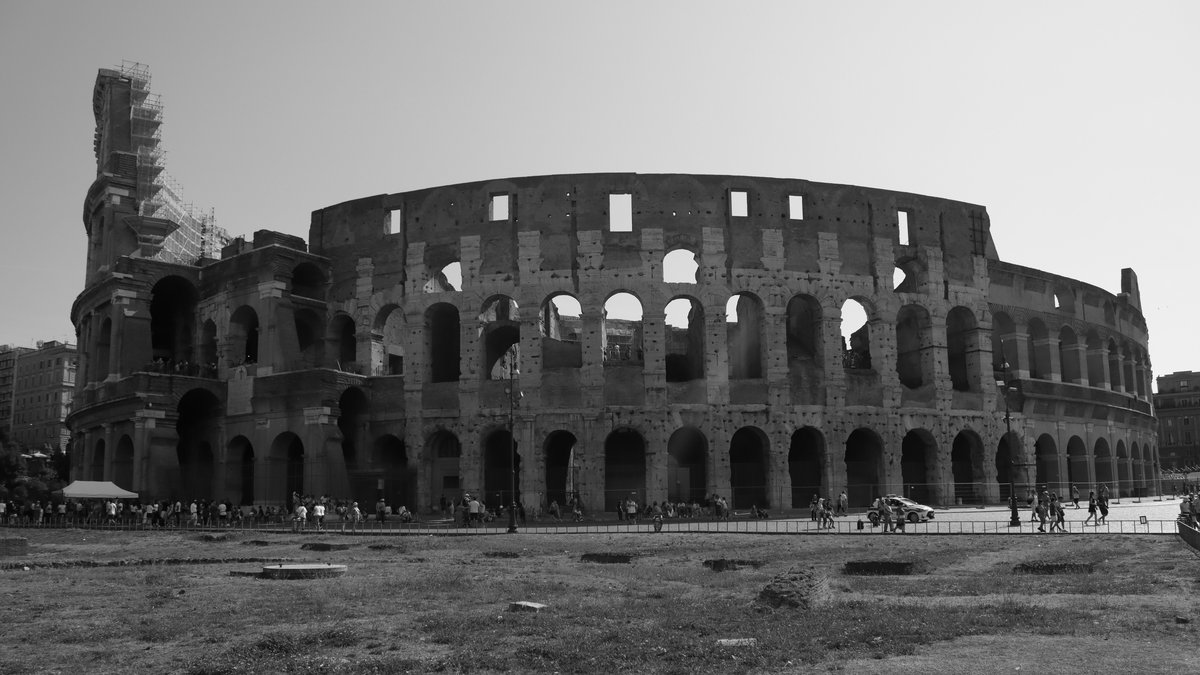 The Colosseum in Rome photographed in black and white, with visitors walking past its arches