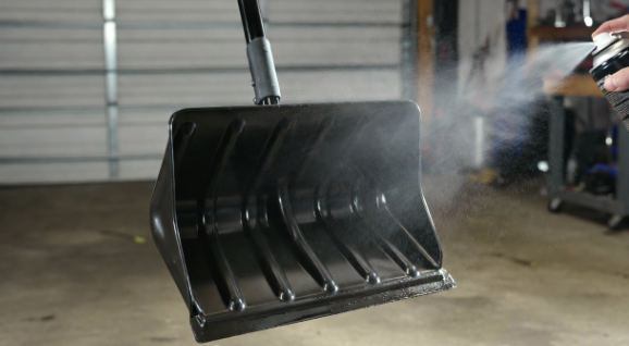 Snow shovel leaning against a garage wall with a can of cooking spray nearby