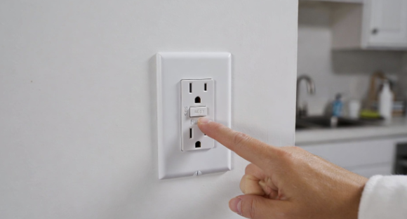 Hand pressing the test button on a GFCI outlet in a kitchen