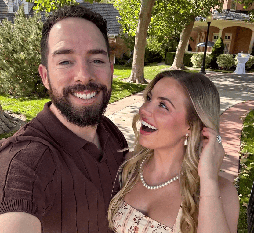 Adam and a woman laughing in a selfie on a sunny garden path