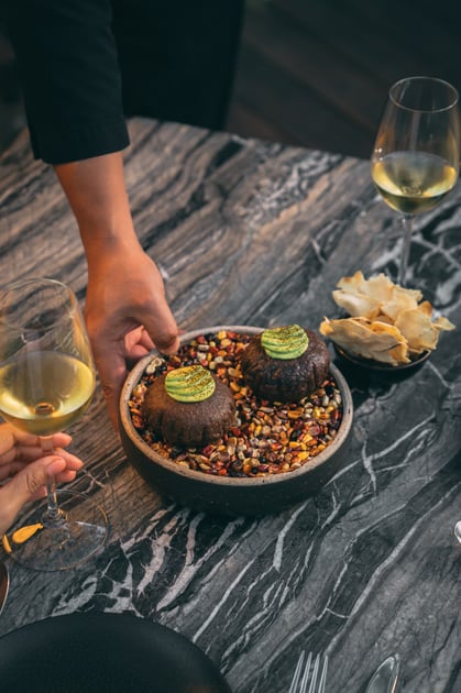 Server presenting a plated dish and wine on a dark stone table