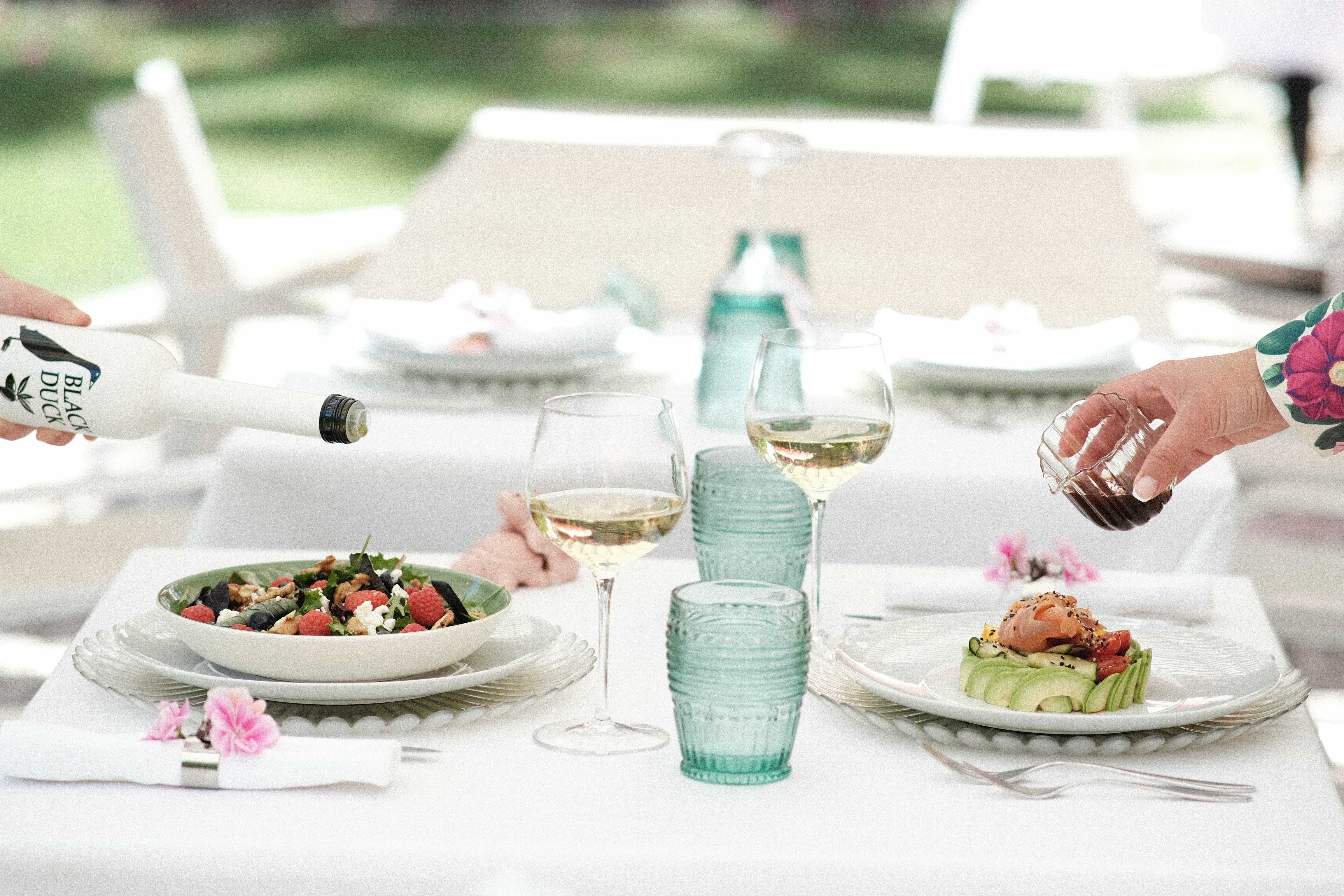 Garden dining table set with salads, glassware, and turquoise bottles
