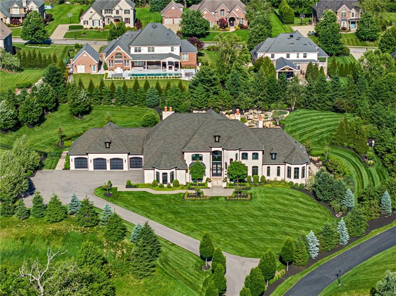 Aerial drone photo of 435 Myoma Road: a sprawling cream-and-grey stone estate with a six-bay garage, a long private drive, striped lawns and rows of evergreens, dwarfing the large homes around it