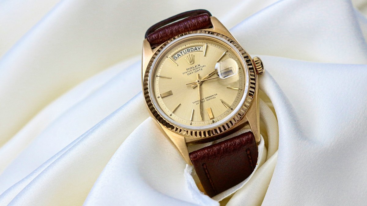 A vintage gold Rolex Day-Date with a brown leather strap resting on white silk