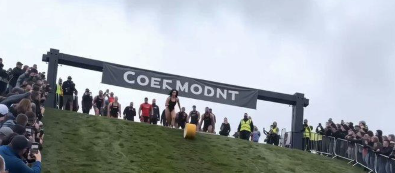 A woman in a swimsuit gliding down a hillside in a cheese-rolling race that never happened, past a garbled sign