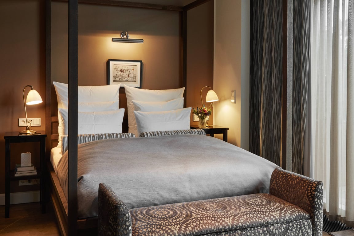 Warmly lit Nimb guest room with a white bed and patterned bench