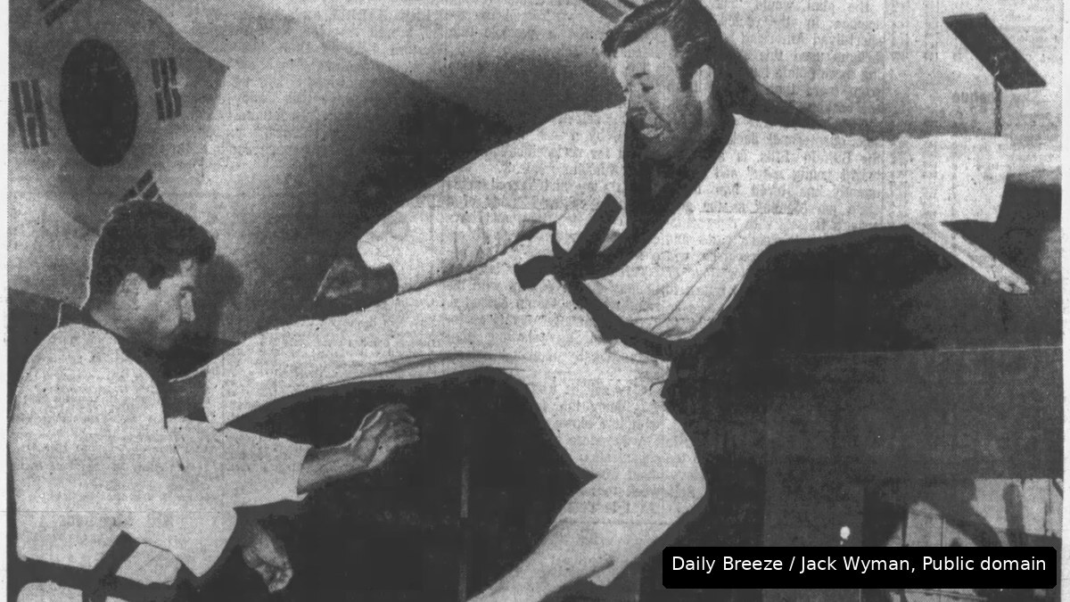 A vintage newspaper photo of a young Chuck Norris mid-air in a flying side kick in a karate school