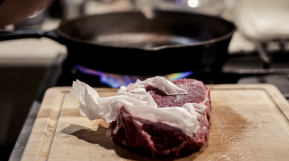 Raw steak being patted dry with paper towels on a cutting board