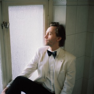 Sondre Lerche i vit kavaj och fluga, sittande vid ett fönster
