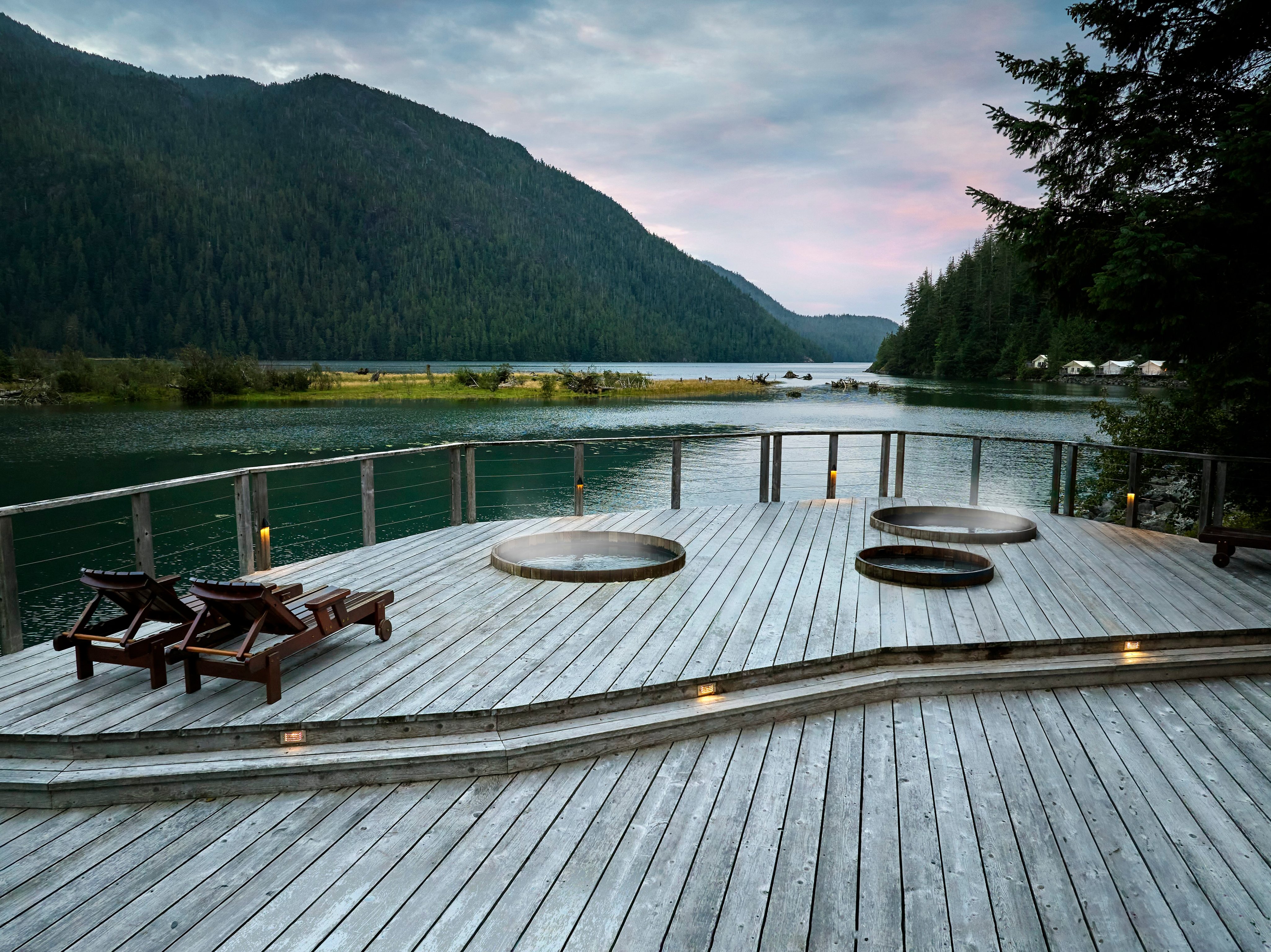 Waterfront cedar deck with hot tubs, loungers, forest, and mountain views