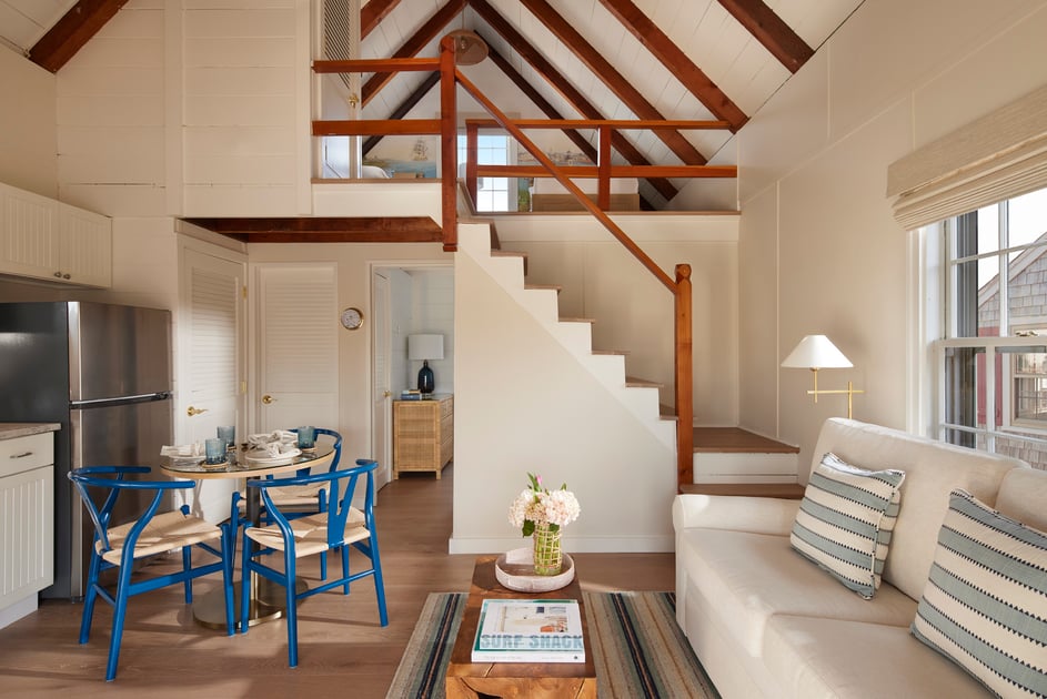 Bright cottage living and dining area with exposed beams and blue chairs