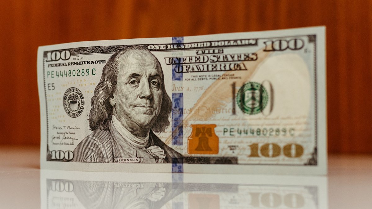 A hundred dollar bill standing upright on a polished table