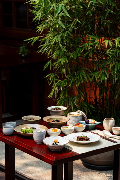 Sichuan dishes and tea arranged on a low table beside bamboo