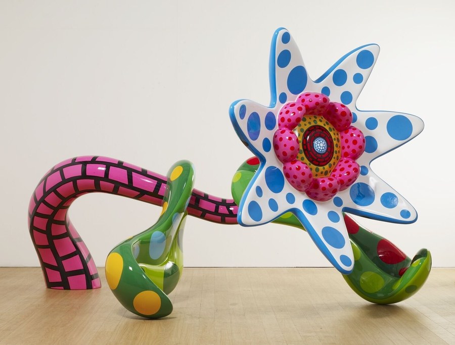 A large polka-dot flower sculpture in pink, green, blue and white standing in a gallery