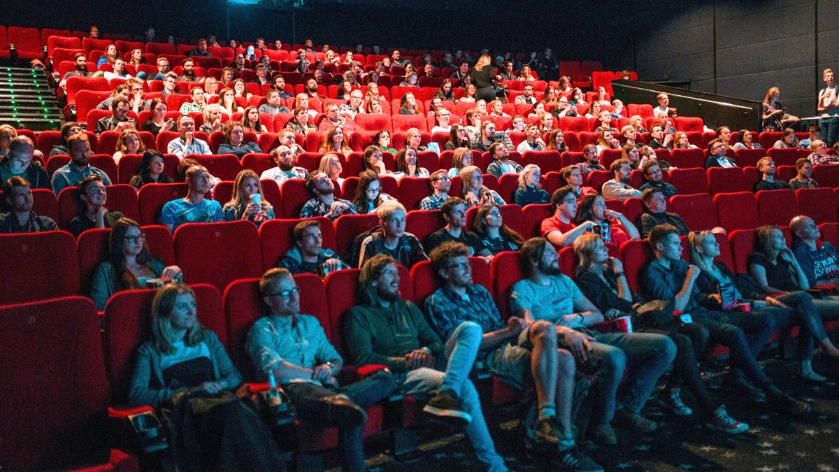 A packed cinema audience in red seats watching a film
