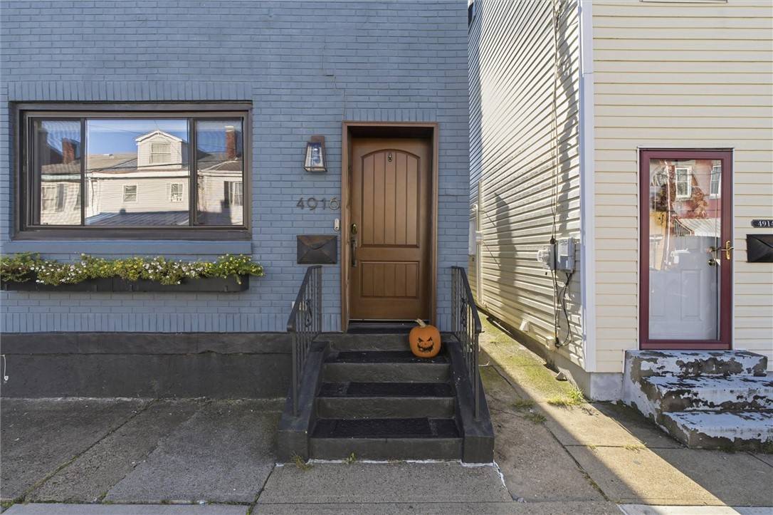 The front of 4916 Hatfield Street: blue-gray brick, a wood front door, a flower box under the window, and a carved jack-o’-lantern on the steps