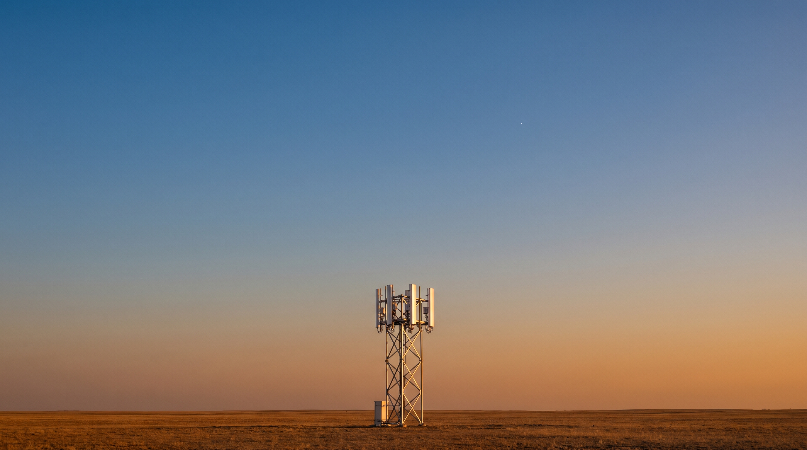 A lone modern cell tower at golden dusk under a wide clear sky