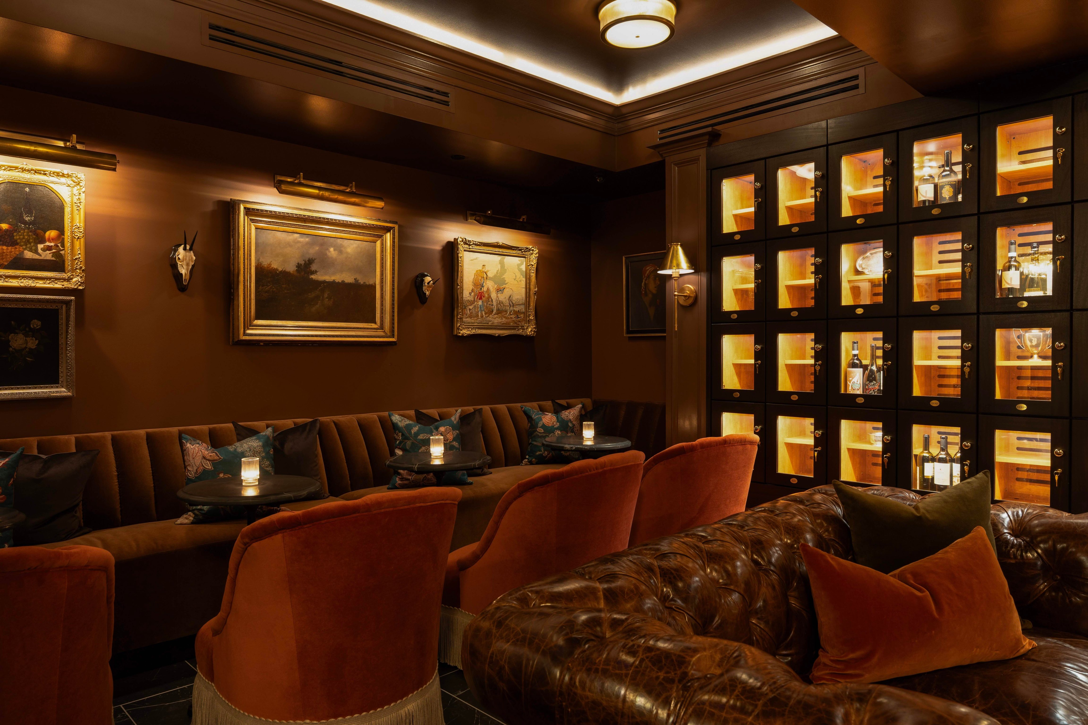 Dark wood private lounge with framed art, red chairs, and a leather banquette