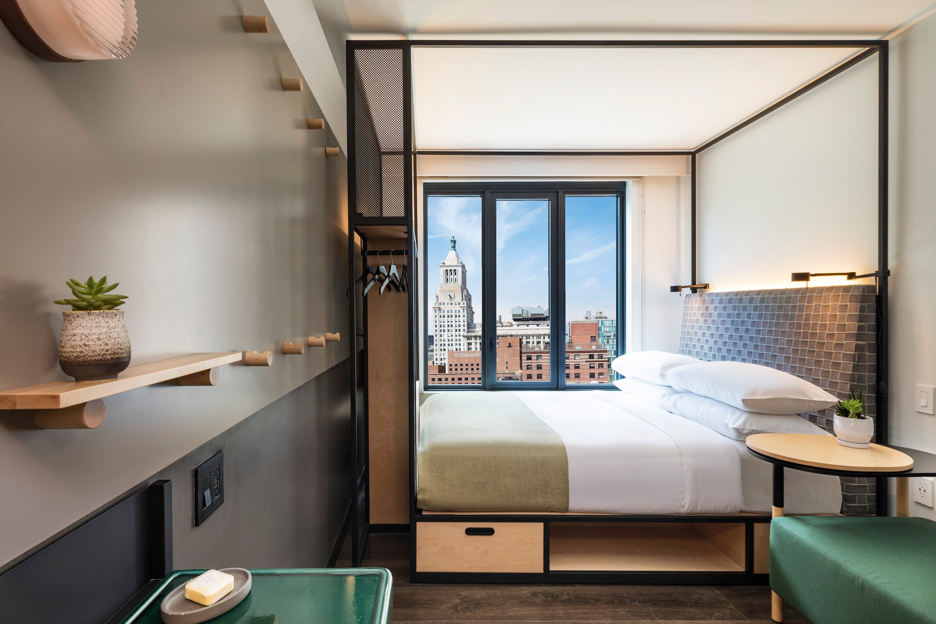 Compact guest room with a black canopy bed and city views