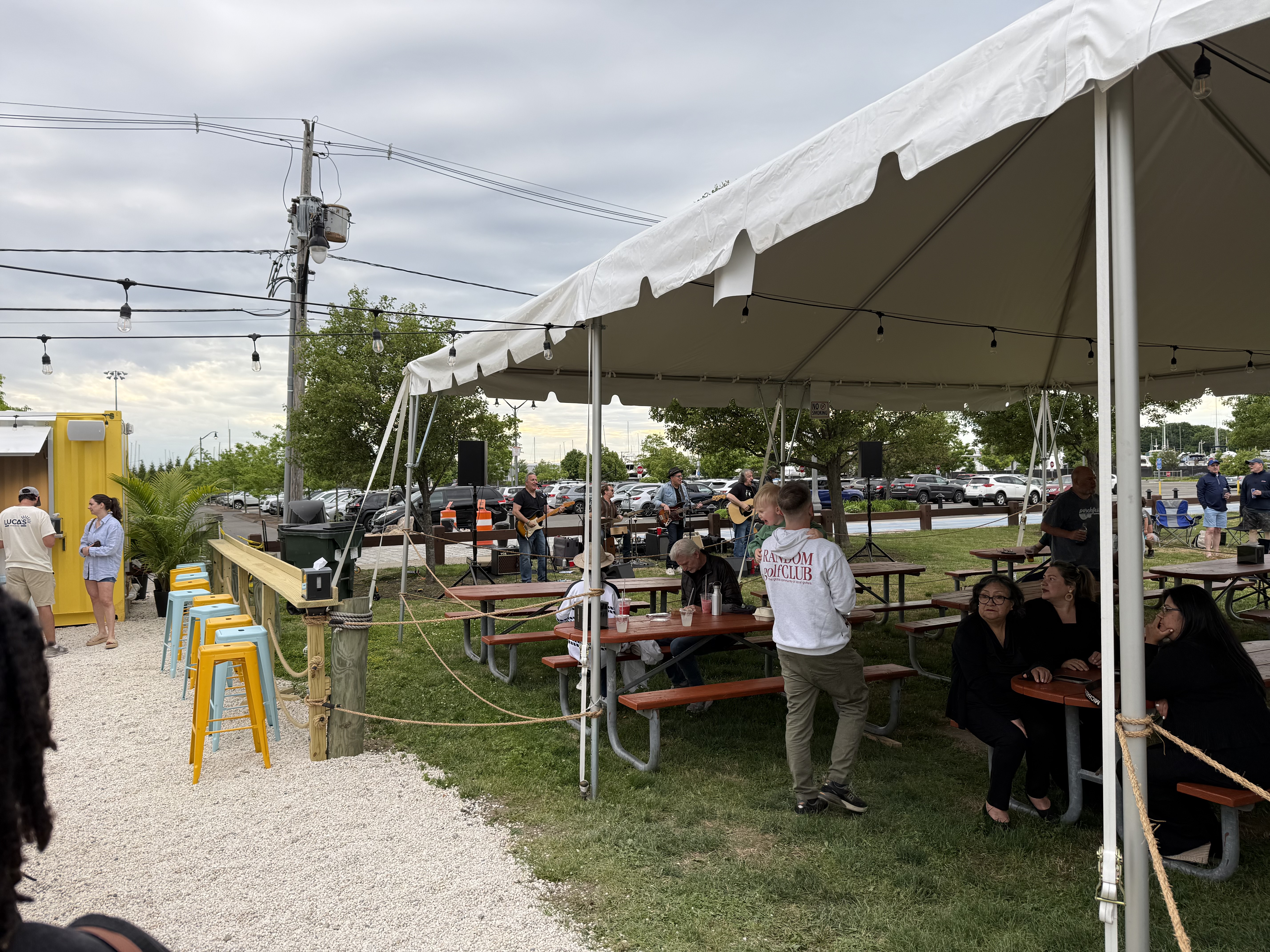 Live music under a tent at Luca's Beach Kitchen with picnic tables and the marina in the background.
