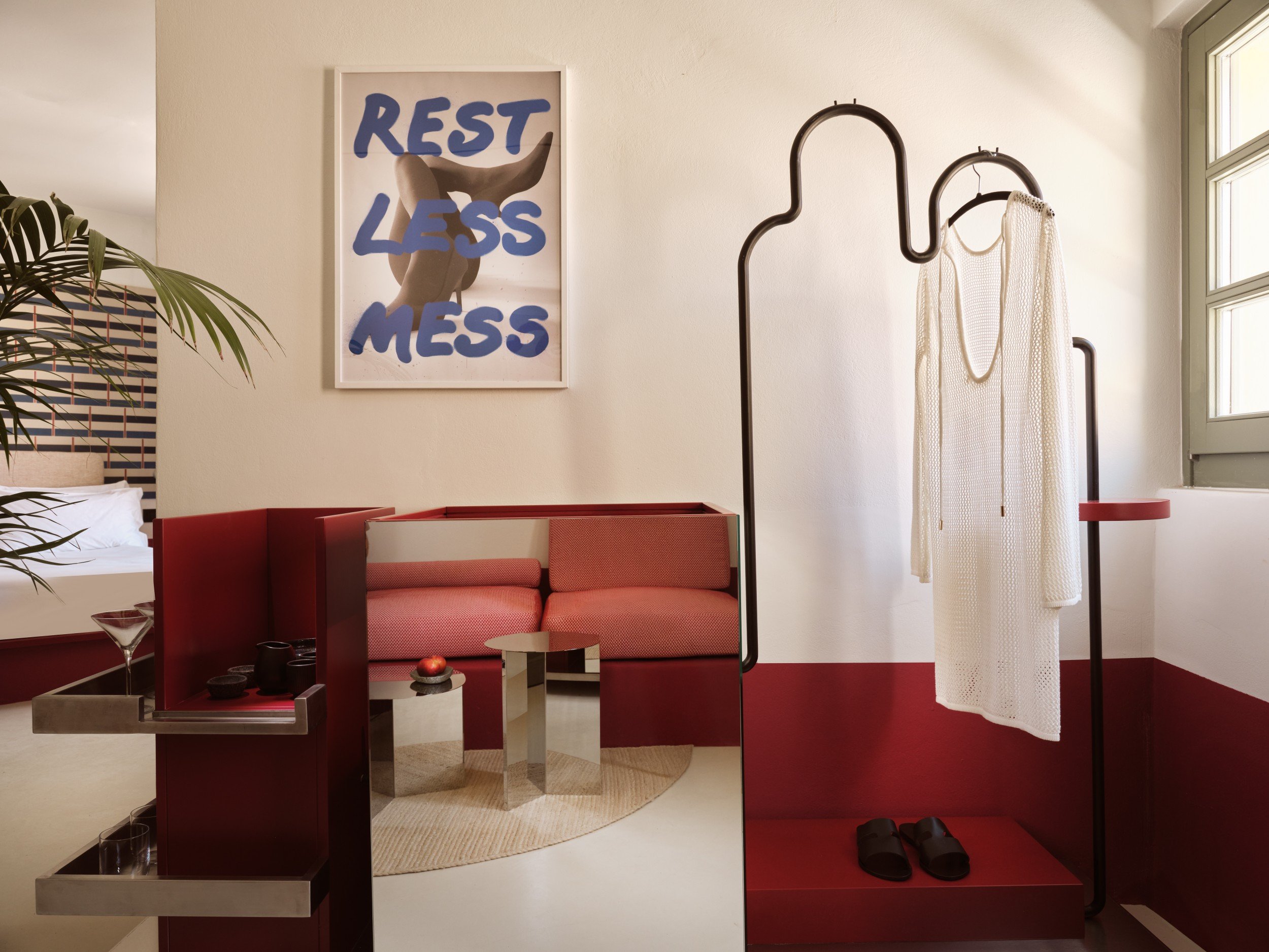 Open wardrobe and red banquette beneath colorful artwork reading Rest Less Mess