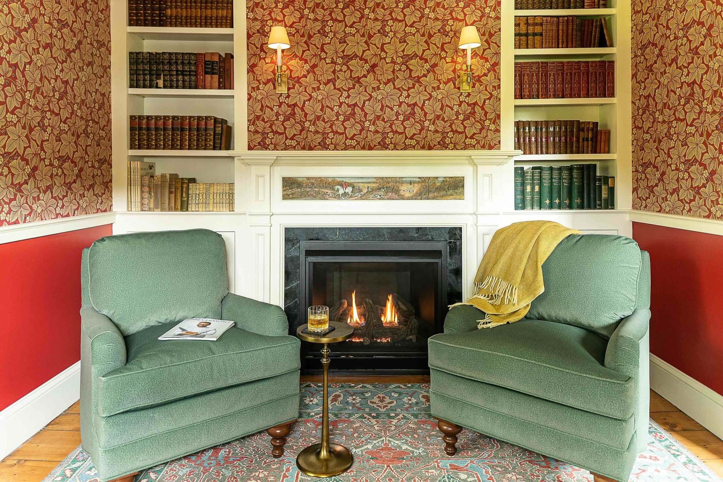 Green armchairs and a fireplace framed by patterned wallpaper at The Weston