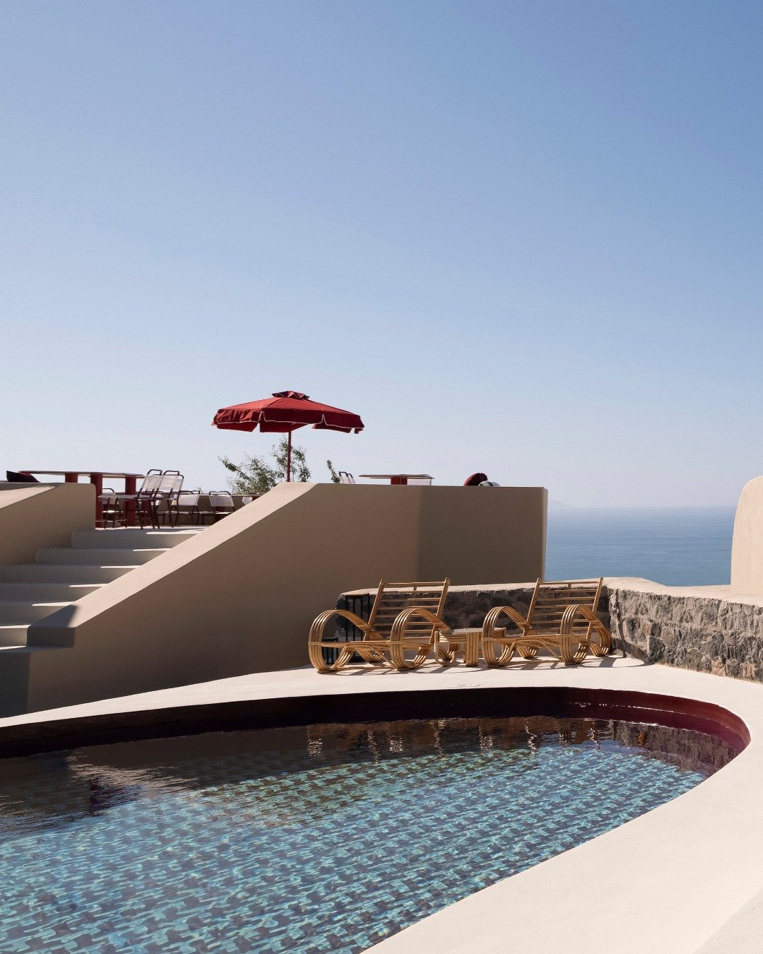 Small tiled plunge pool with loungers and a red umbrella overlooking the sea