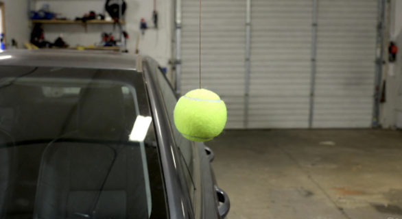 Tennis ball hanging from string in garage touching a car windshield