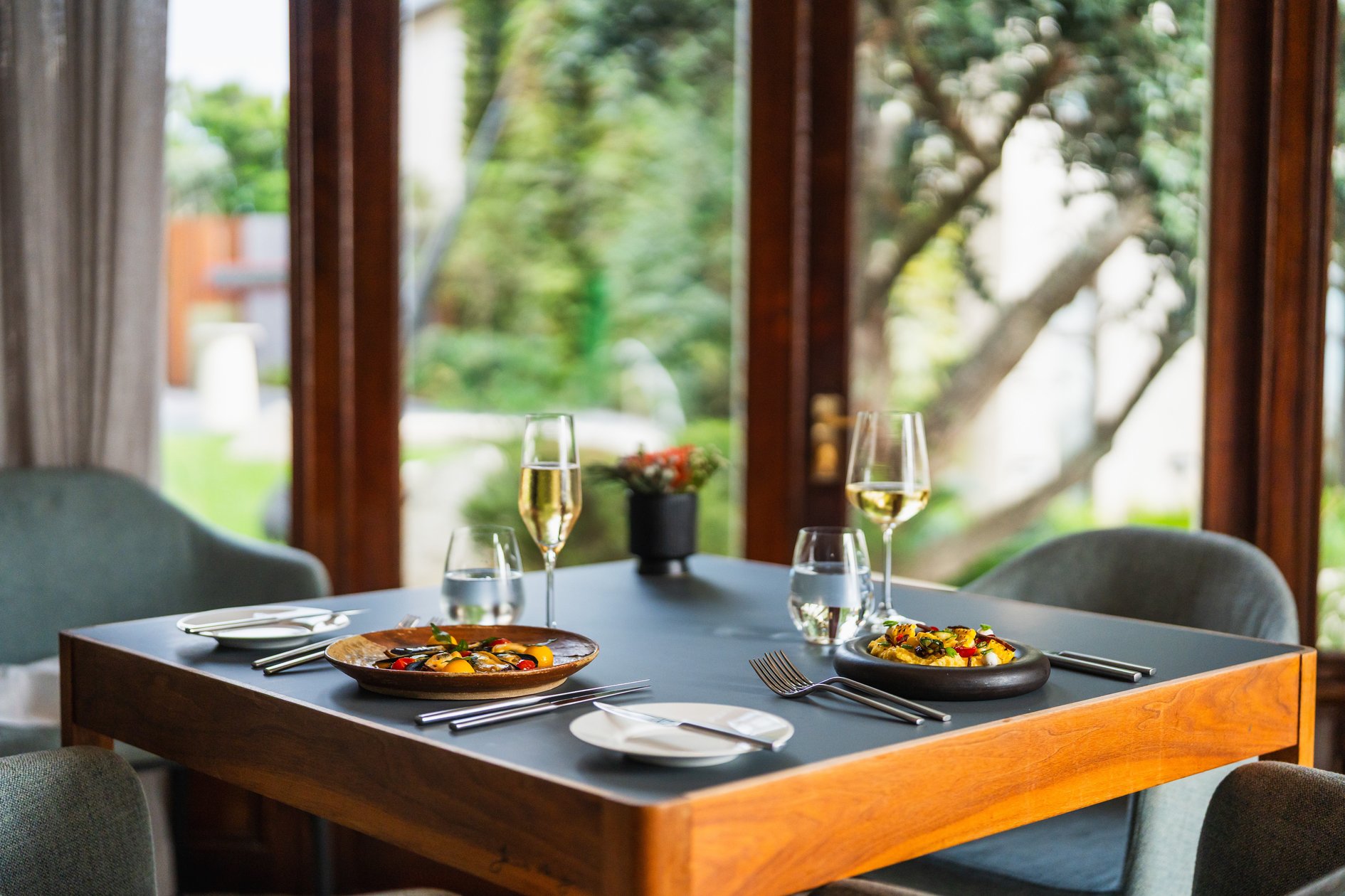 Intimate dining table set beside windows overlooking the garden