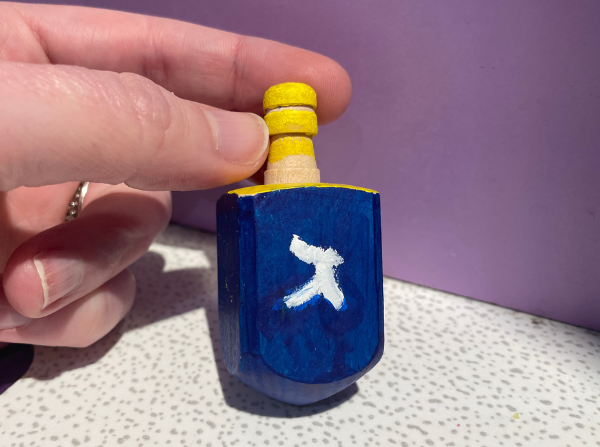 A hand holding a blue and yellow dreidel in the LICM Hanukkah craft image